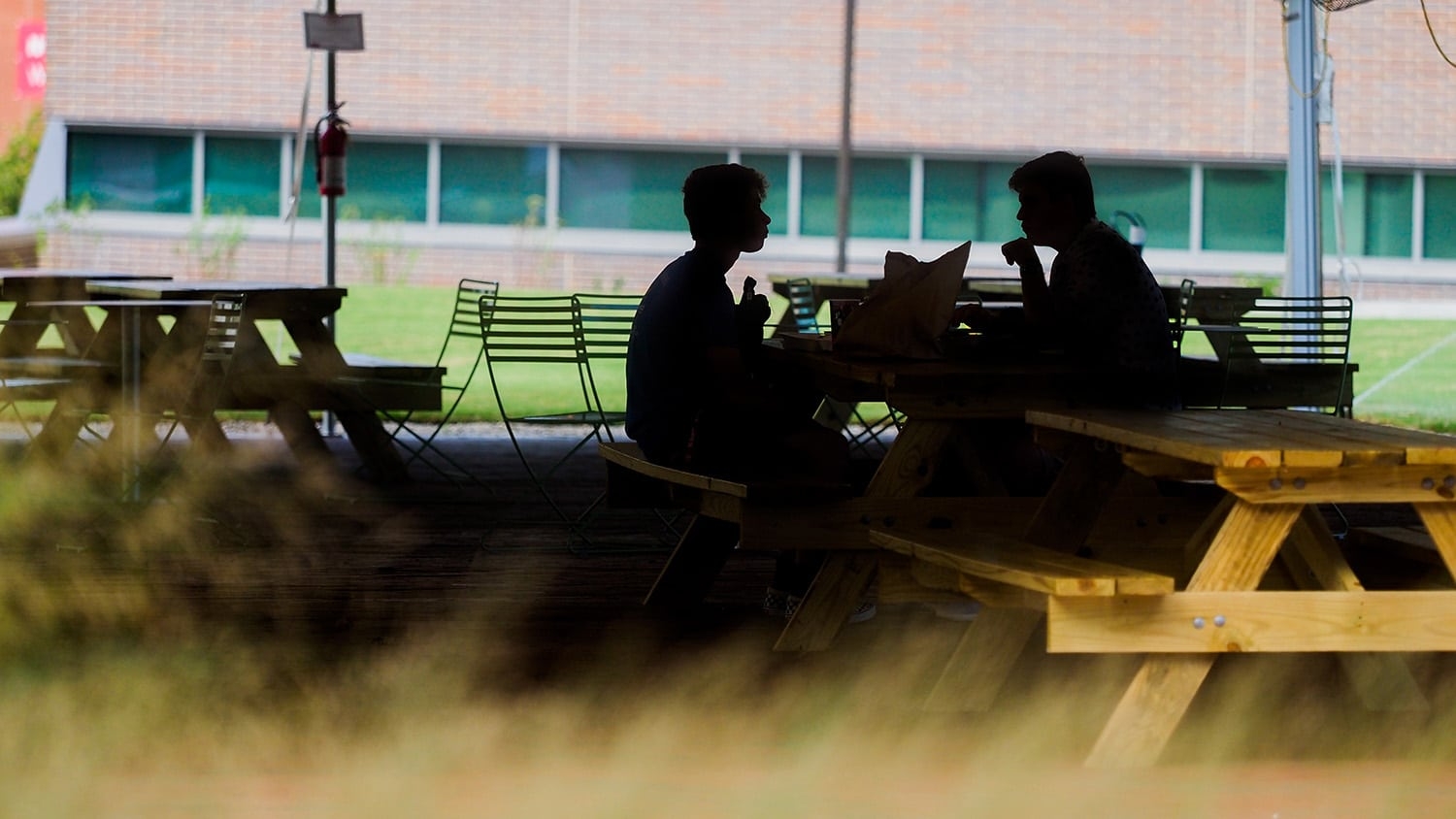 Two people, in shadows, talk at a picnic table on NC State's campus
