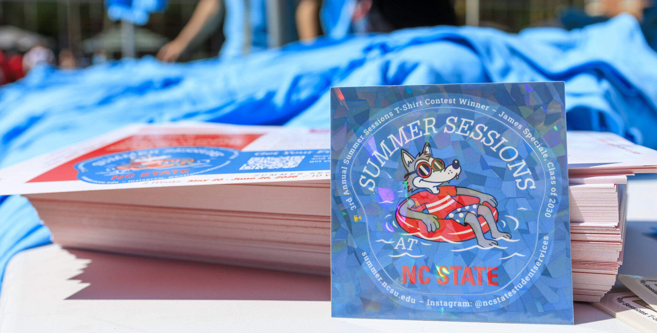 Sticker for the Summer Sessions Campaign, depicting an illustrated anthropomorphic wolf floating on an innertube on water. Surrounding the wolf is text stating "Summer Sessions Fest, NC State".